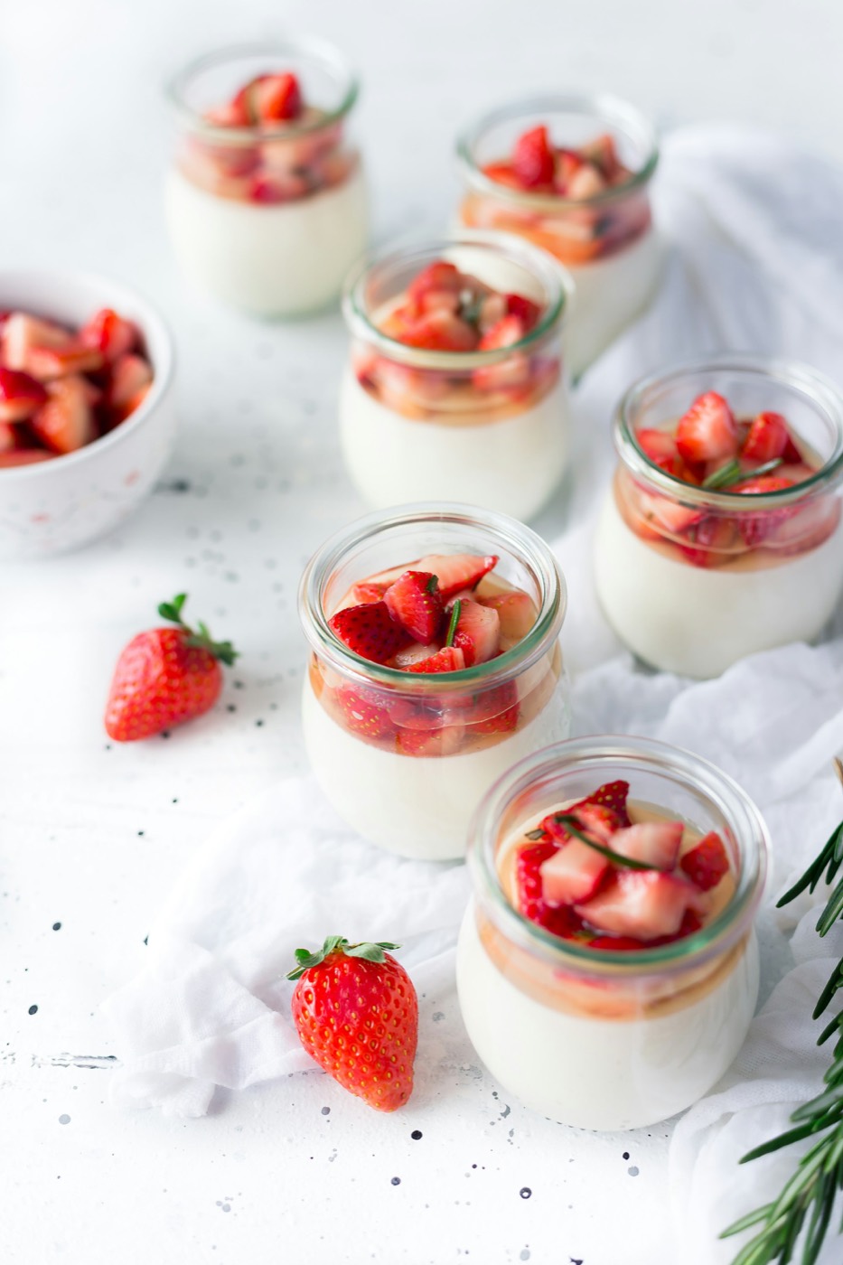Small glass jars of cream topped with chopped strawberries