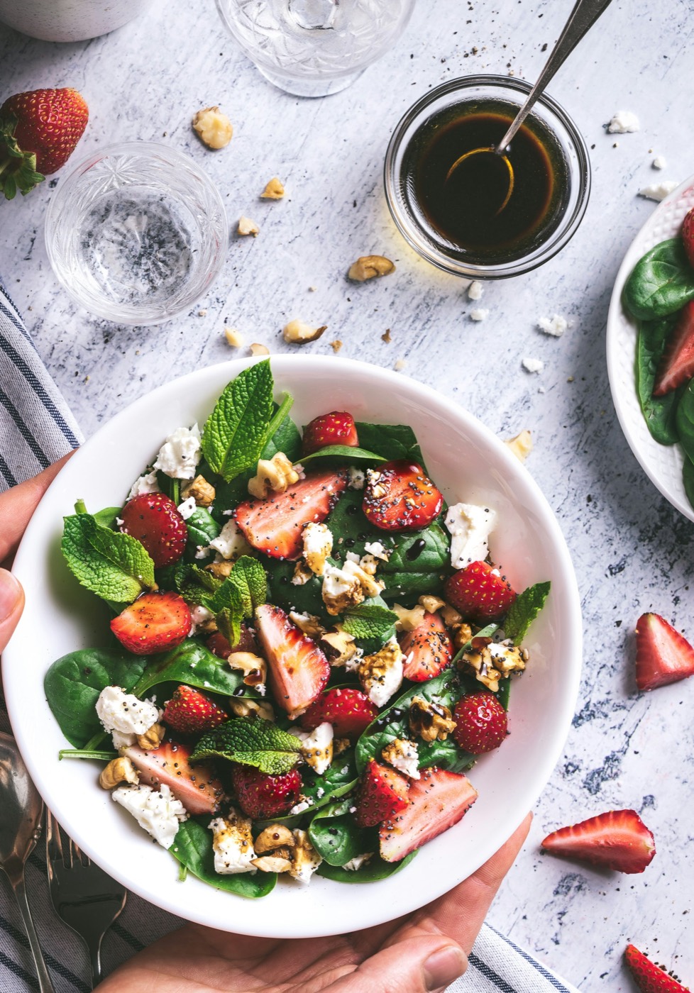 A bowl of spinach salad with sliced strawberries and crumbled cheese