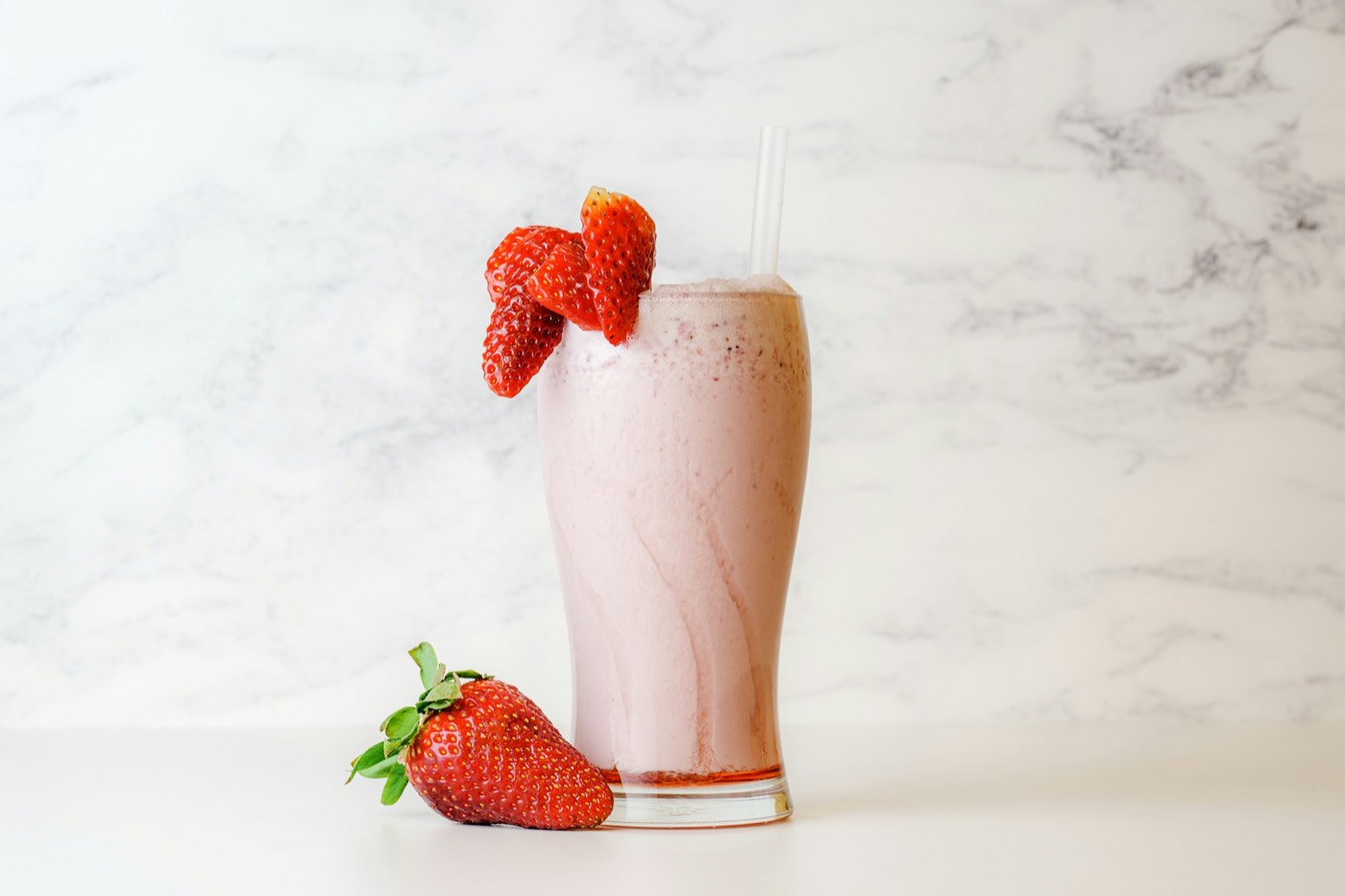 A glass of pink strawberry lassi with a strawberry on the rim