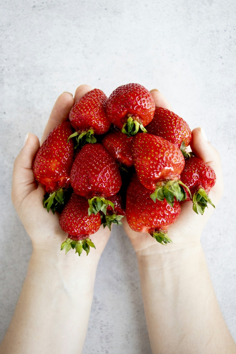 Two cupped hands full of ripe red strawberries